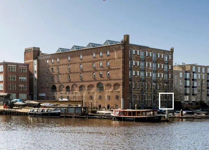 Uitzicht op een historisch pakhuis aan de Hoogte Kadijk in Amsterdam met woonboten aan de kade.